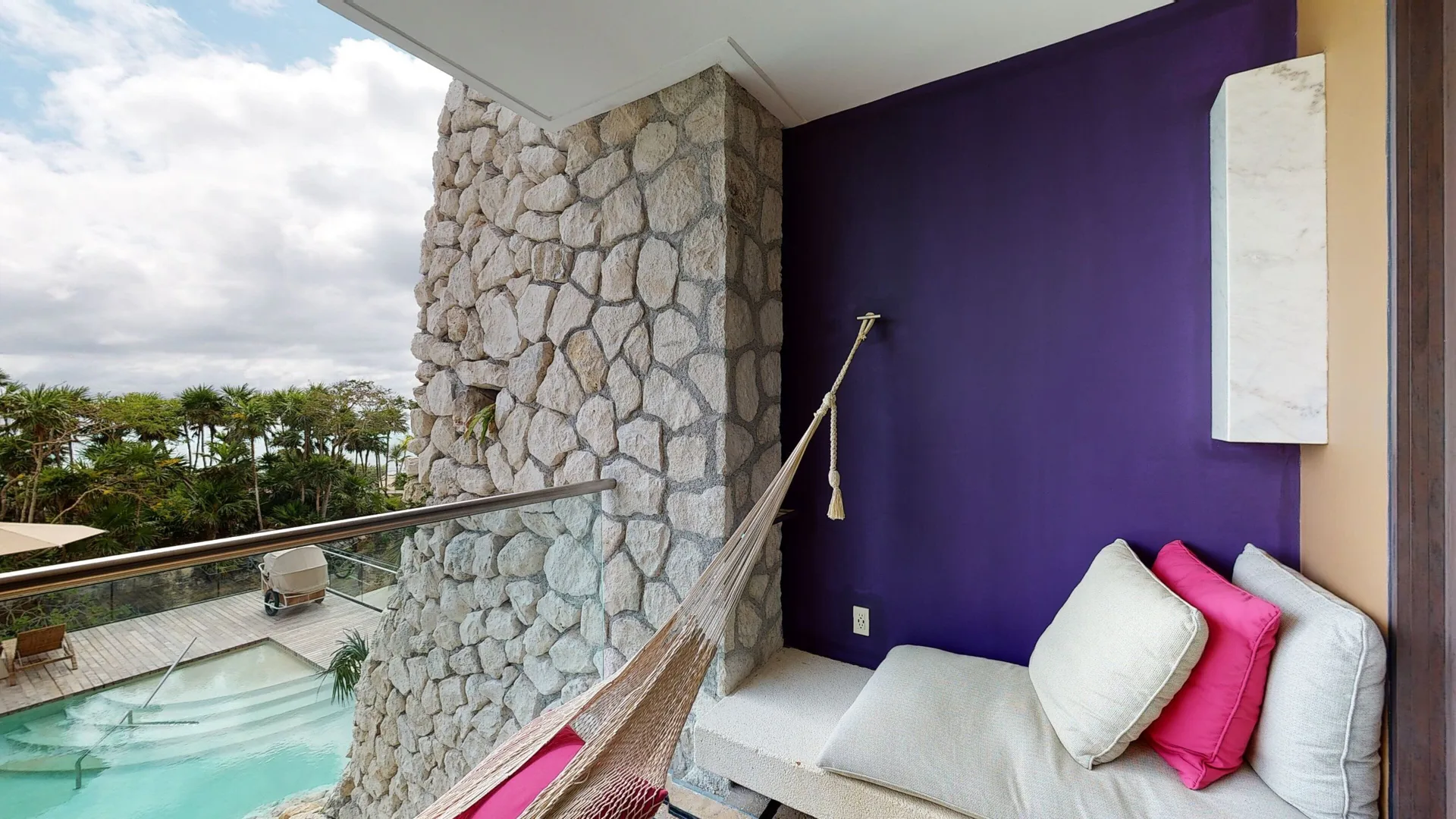 Oceanfront suite balcony at Hotel Xcaret Arte with hammock, daybed and pool view.