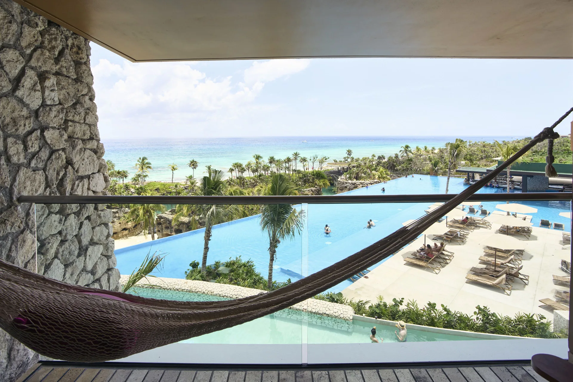 Oceanfront suite balcony at Hotel Xcaret Arte with hammock overlooking pool and sea.