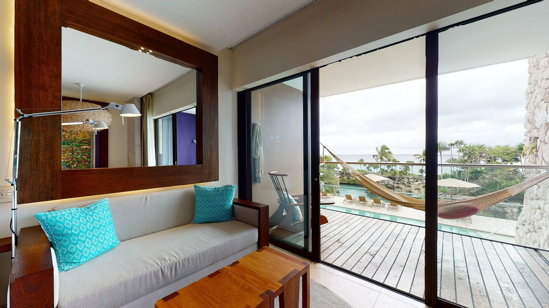 Oceanfront suite sitting area at Hotel Xcaret Arte with sofa, mirror and balcony hammock.