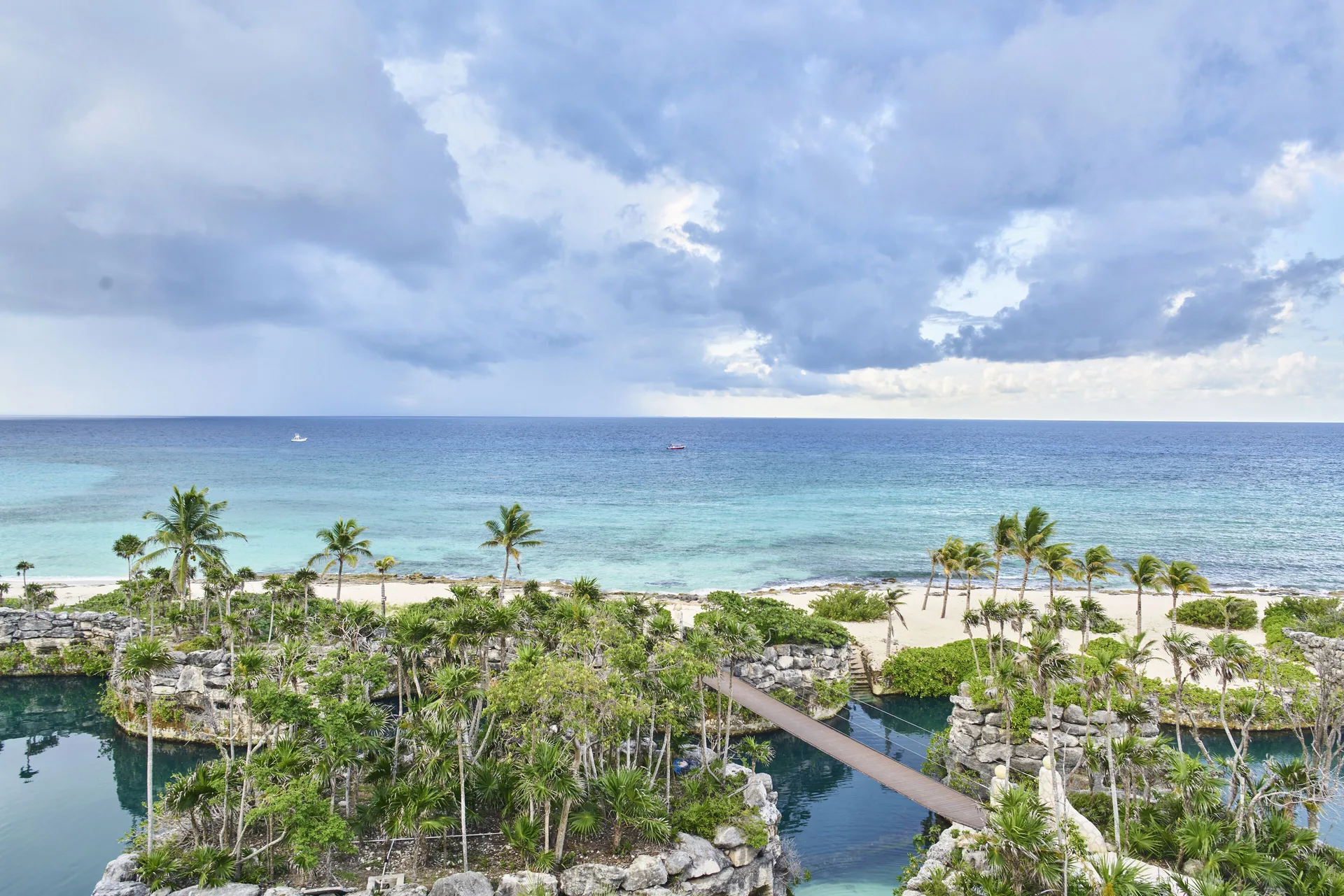 Oceanfront view from a suite at Hotel Xcaret Arte with beach, palms, lagoons and cloudy sky.