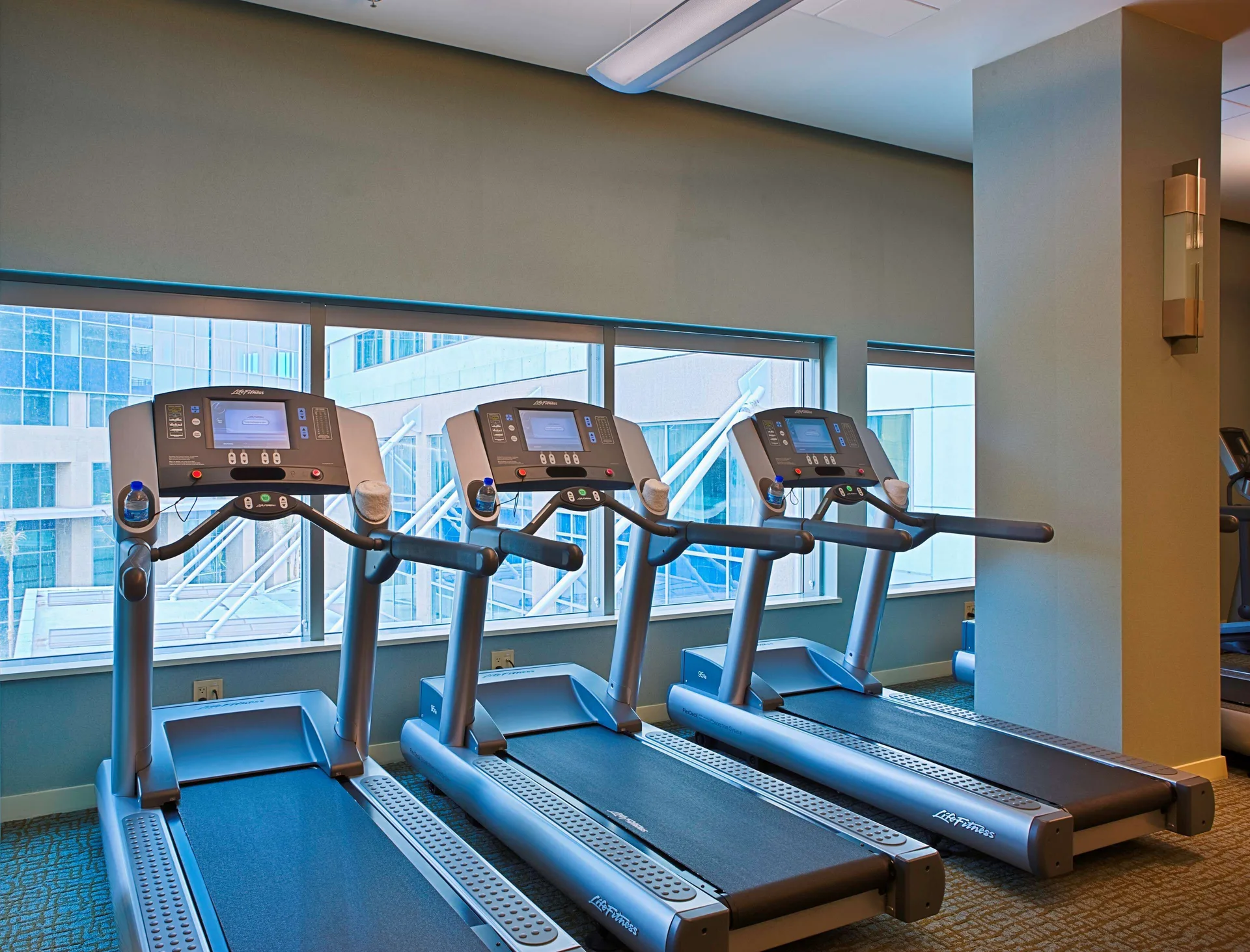 Three treadmills lined up by large windows at Hyatt Regency Trinidad.