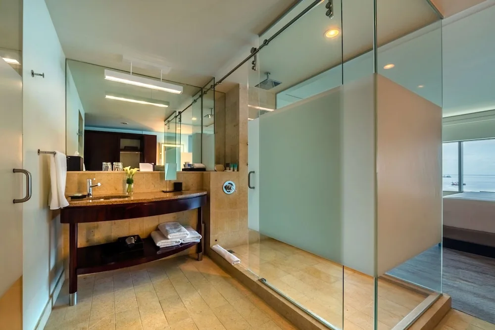 Glass shower, vanity and bedroom beyond in a guest bathroom at Hyatt Regency Trinidad.