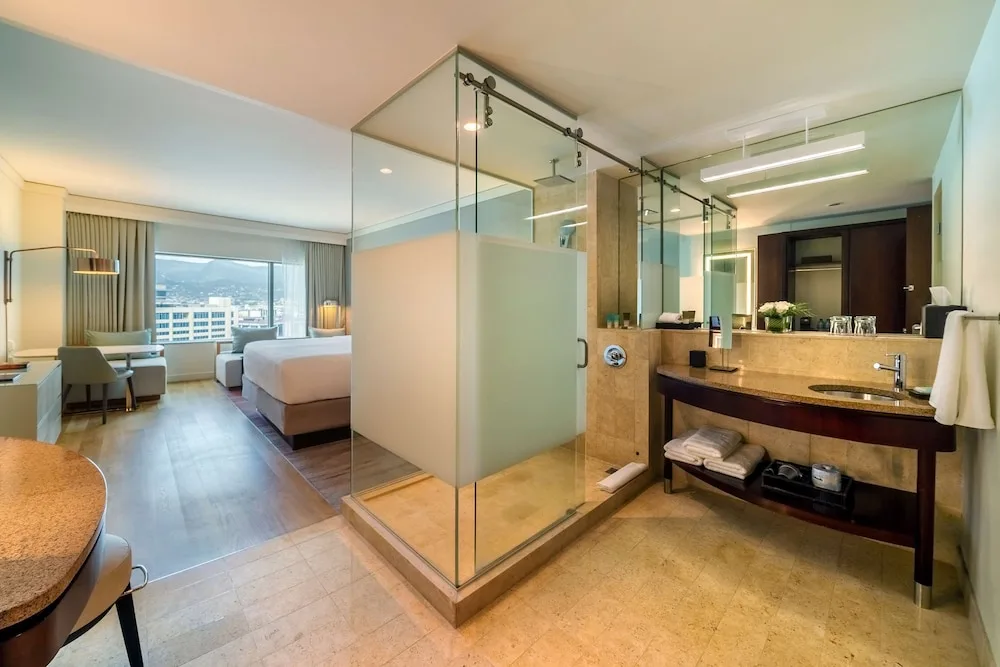 Guest room bathroom with glass shower and bedroom beyond at Hyatt Regency Trinidad.