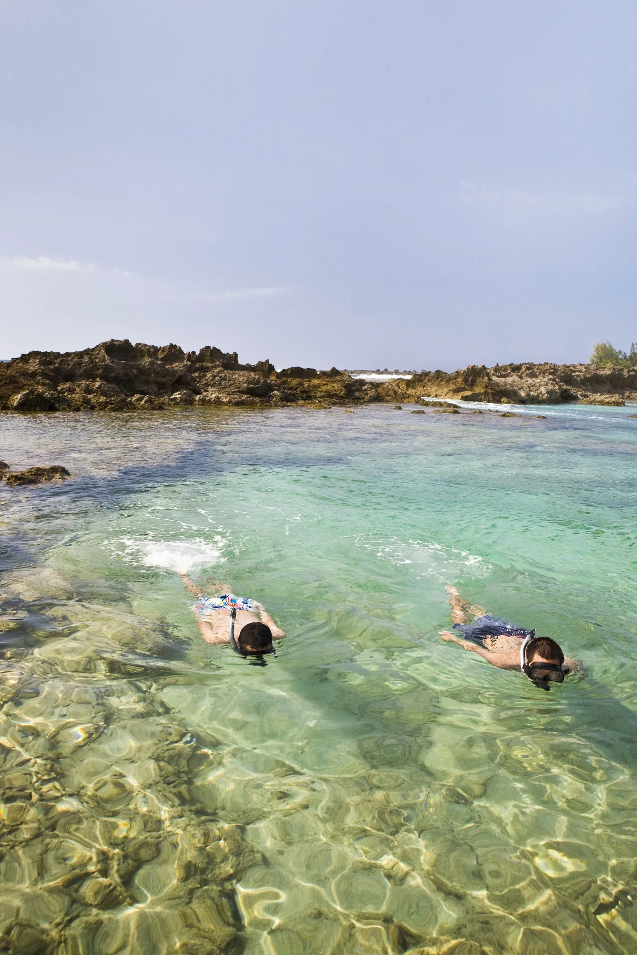 Two snorkelers in clear turquoise water near lava rock at Hyatt Regency Waikiki Beach Resort & Spa.