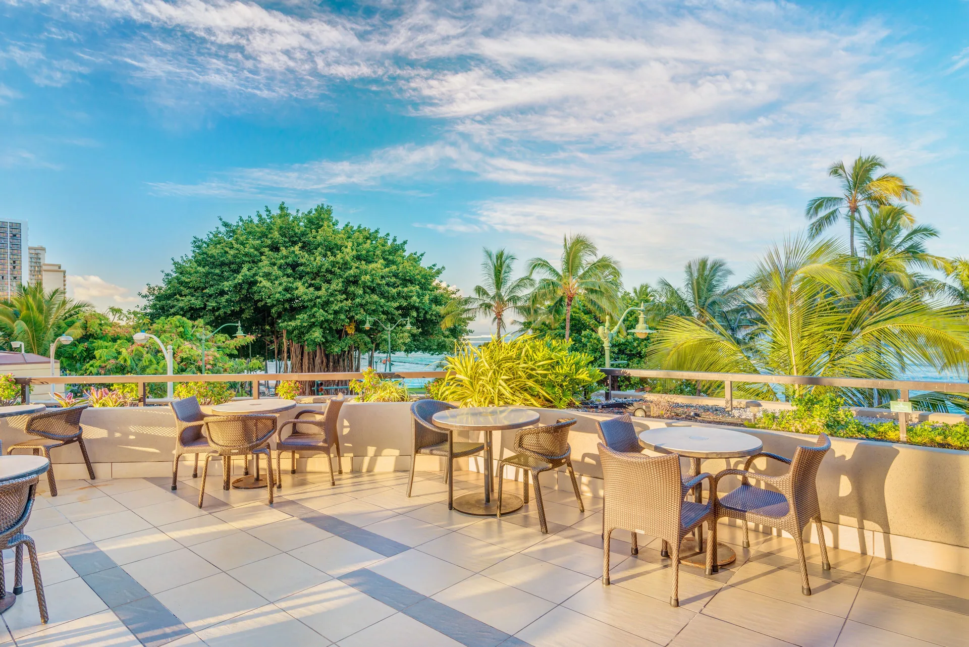 Outdoor terrace seating with palm trees and ocean beyond at Hyatt Regency Waikiki Beach Resort & Spa.