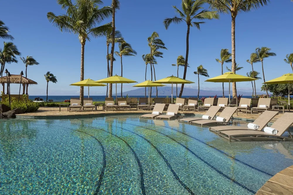 Pool loungers and yellow umbrellas by the ocean at Hyatt Vacation Club at Ka'anapali Beach.