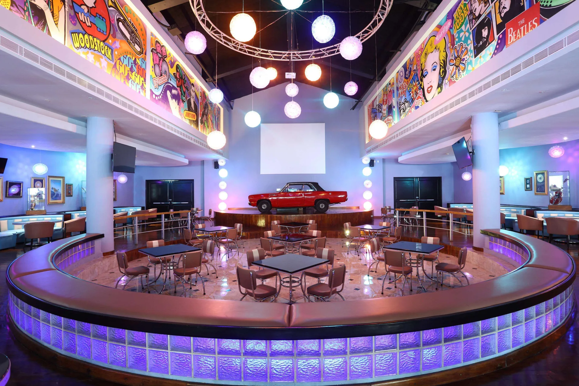 Retro nightclub with stage, red car, and colorful lights at Iberostar Waves Paraíso del Mar.
