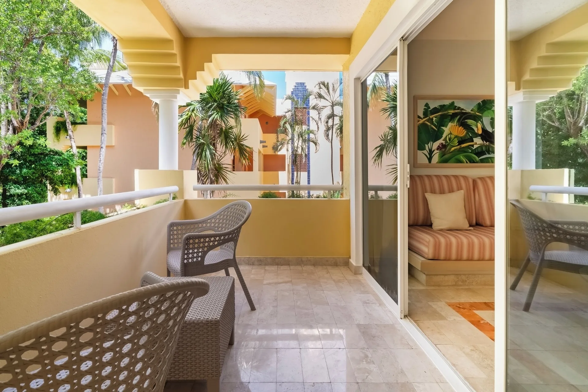 Junior Suite balcony at Iberostar Waves Paraíso del Mar with chairs, trees, and sliding doors to the room.
