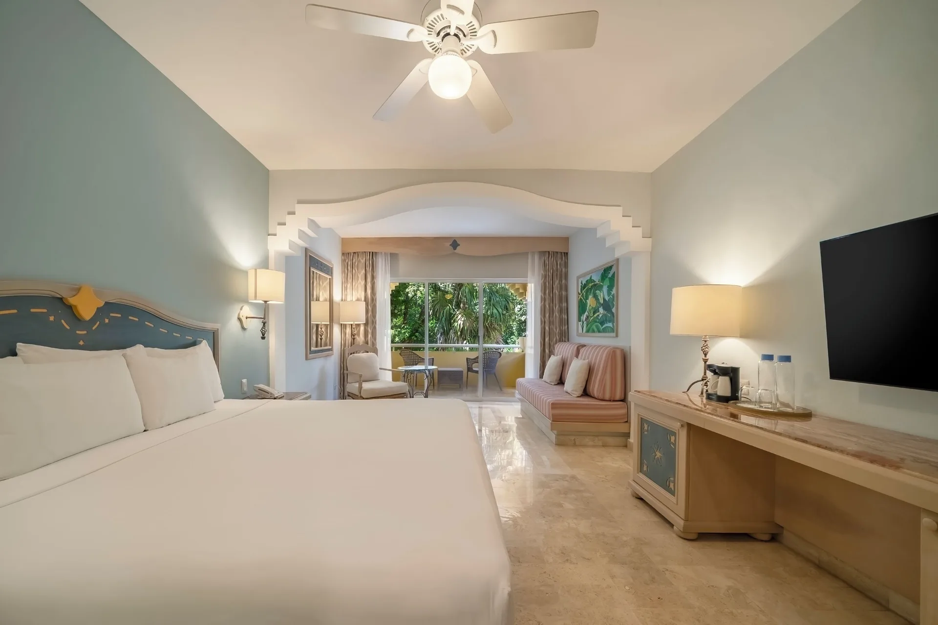 Junior Suite king bed at Iberostar Waves Paraíso del Mar with TV console, sofa, and balcony beyond.