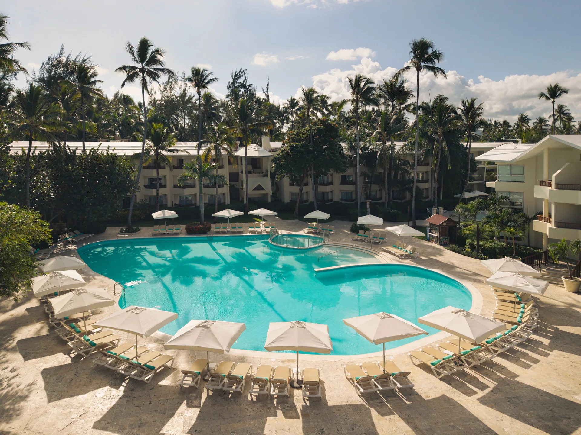 Round resort pool with umbrellas and palm shadows at Impressive Premium Punta Cana.