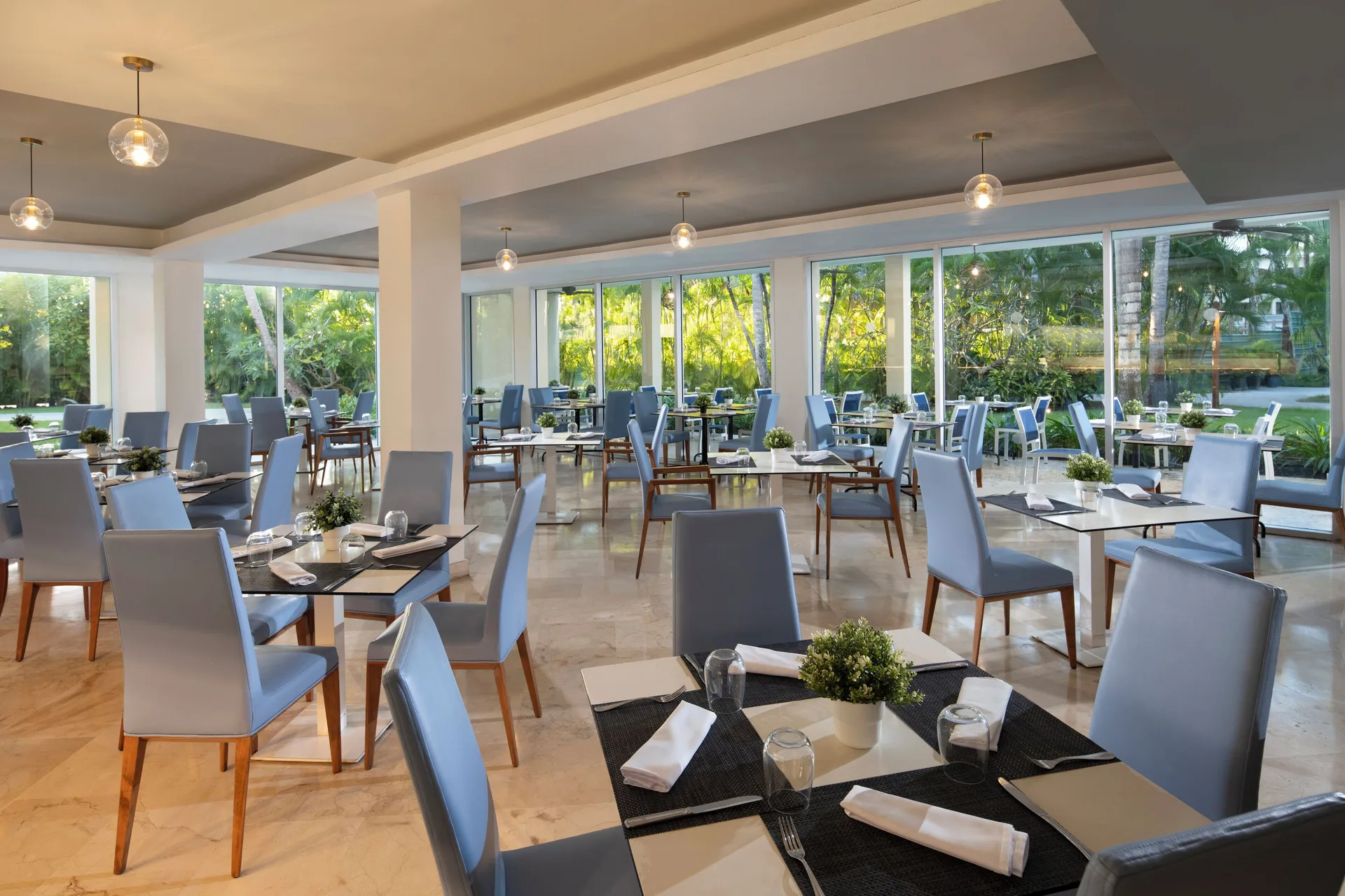 Bright dining room with pale blue chairs and garden windows at Impressive Premium Punta Cana.