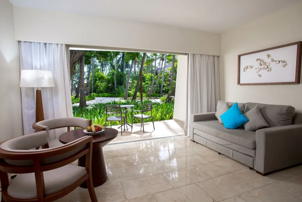 Garden-view sitting area with sofa and patio in a junior suite at Impressive Premium Punta Cana.