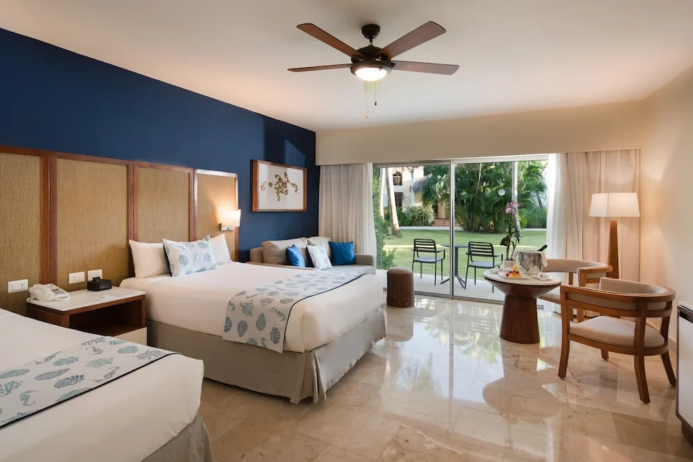Junior suite with two beds, sofa, dining table, and garden patio at Impressive Premium Punta Cana.