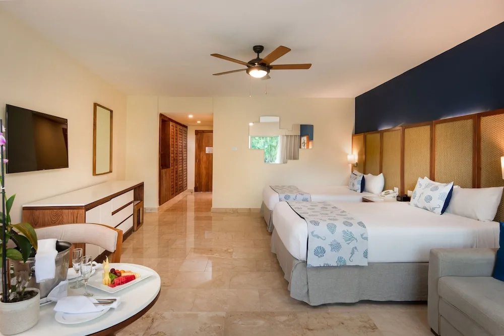 Junior suite with two beds, TV, seating, and entry area at Impressive Premium Punta Cana.