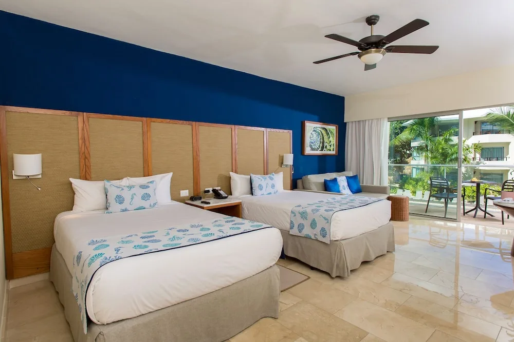 Two beds and a balcony with tropical greenery in a junior suite at Impressive Premium Punta Cana.