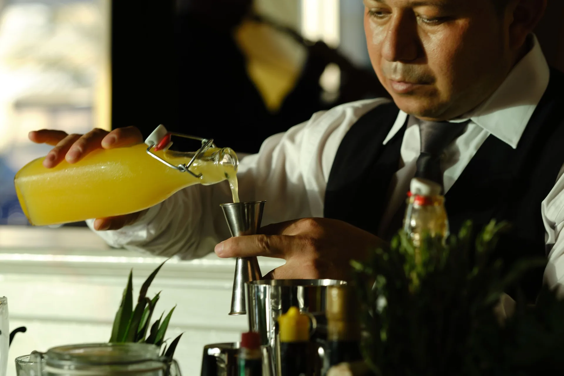 Bartender pours a yellow mixer into a jigger at JOIA Paraíso by Iberostar.