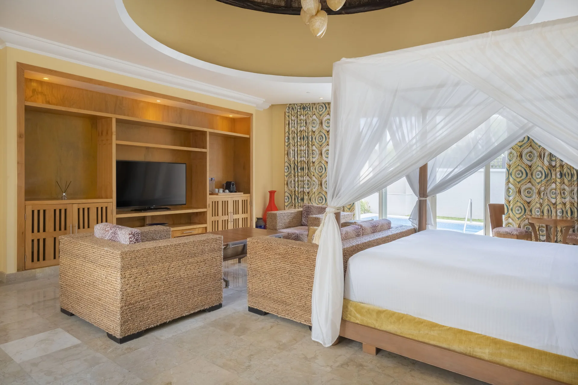 Romantic Villa at JOIA Paraíso by Iberostar with canopy bed, seating area, and private pool beyond glass doors.