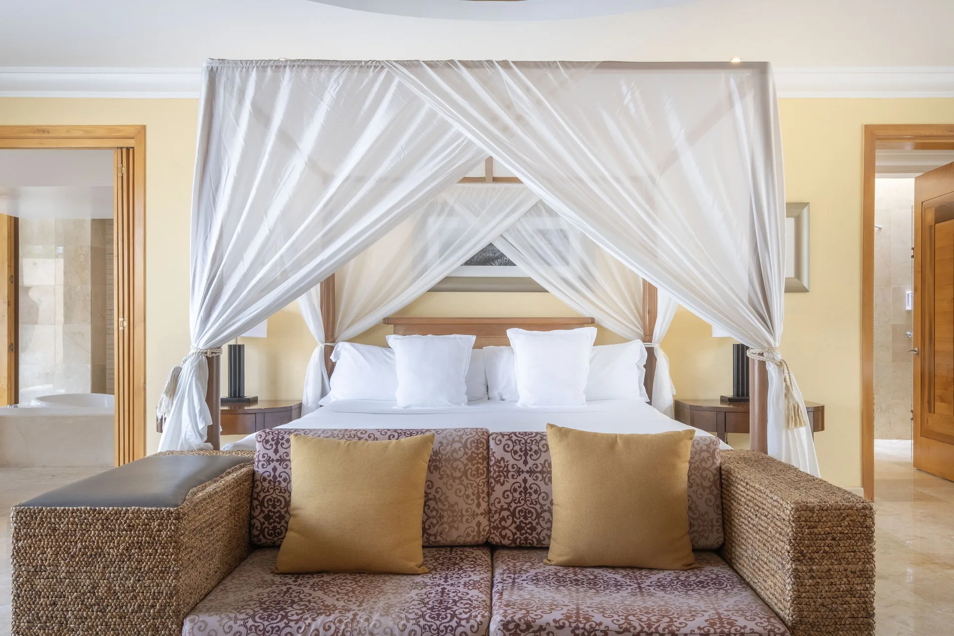 Canopy bed and sofa in a Romantic Villa at JOIA Paraíso by Iberostar with bathroom doorways on both sides.