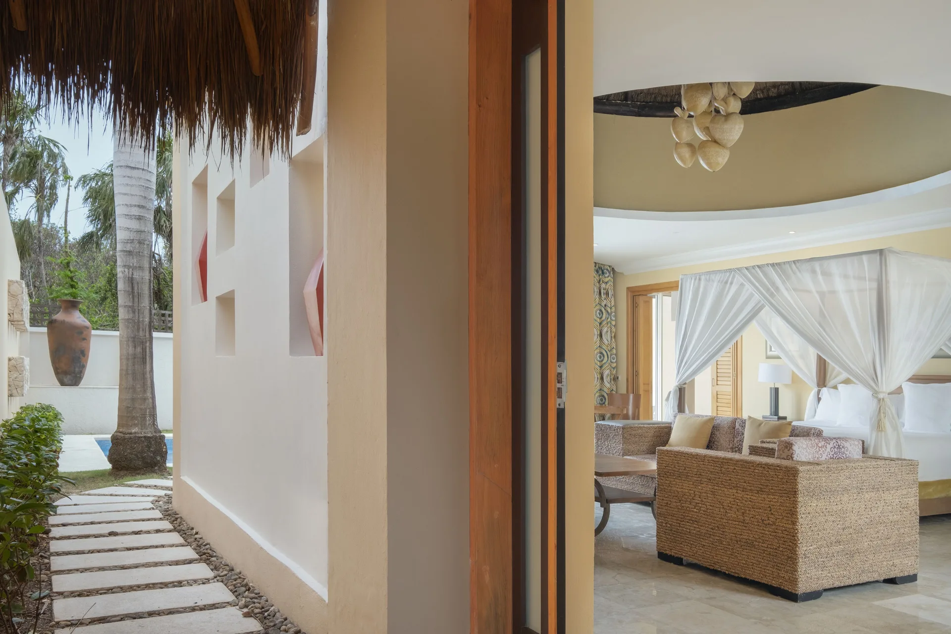 Open doorway to a Romantic Villa at JOIA Paraíso by Iberostar showing the canopy bed and private garden path.