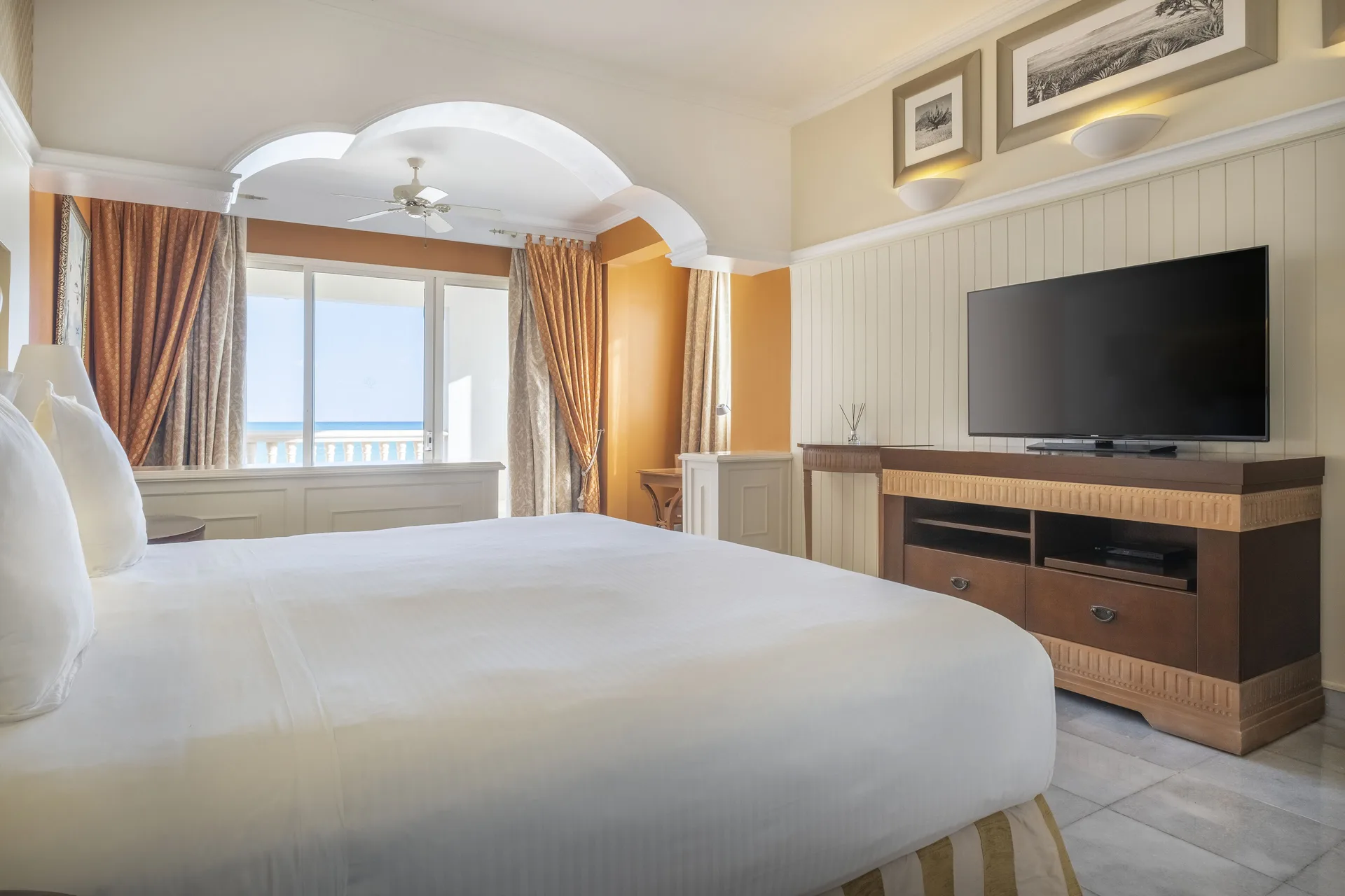 Oceanfront corner suite bedroom with bed and TV at JOIA Paraíso by Iberostar.