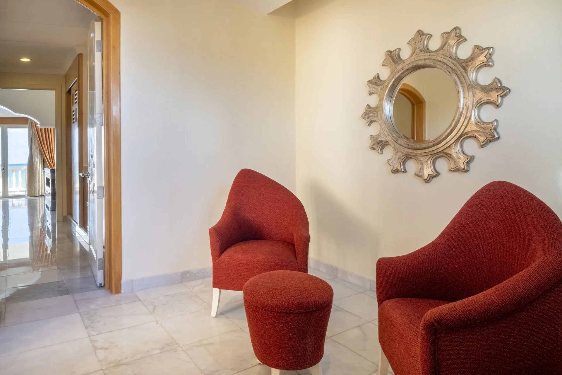 Suite seating nook with red chairs and round mirror at JOIA Paraíso by Iberostar.