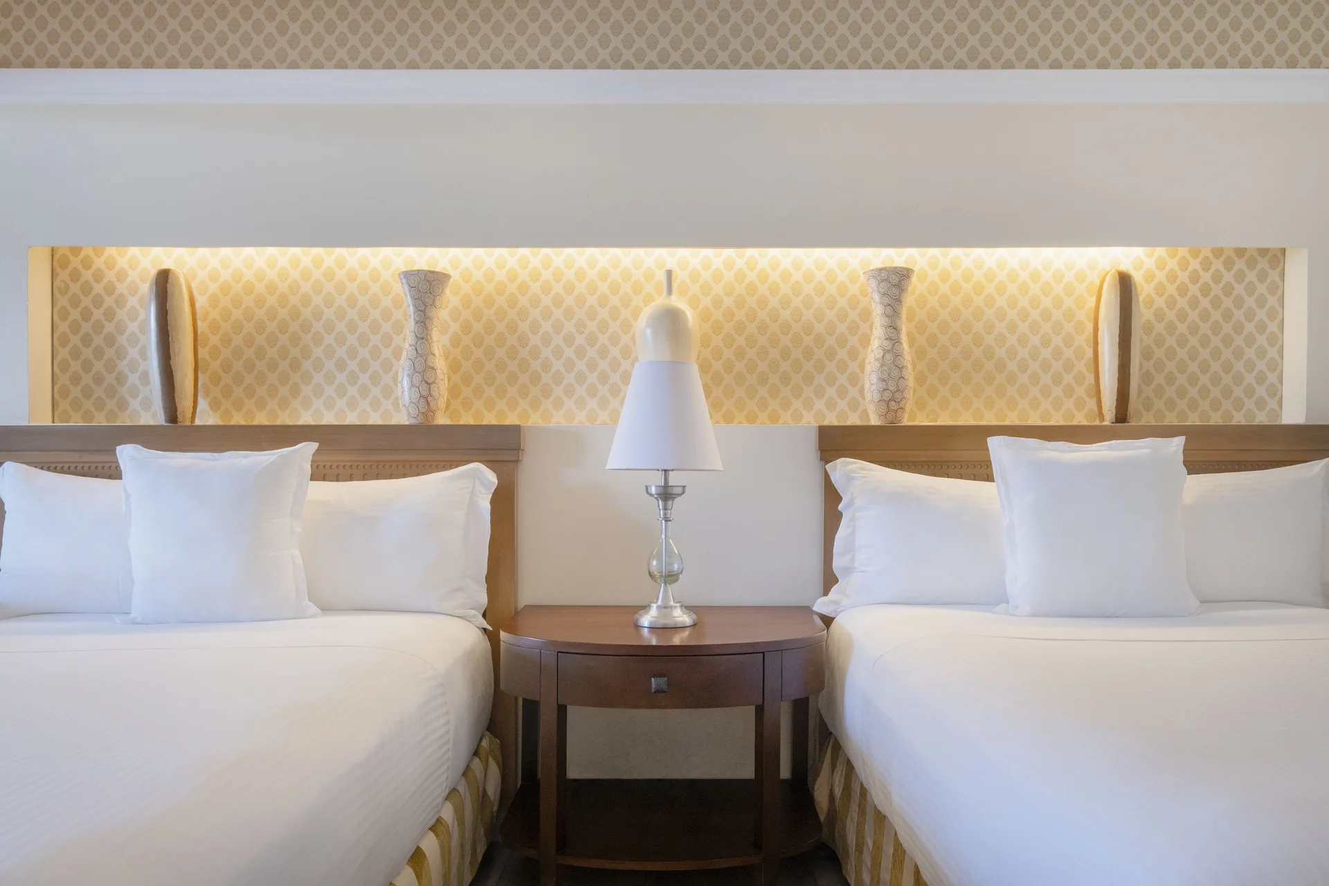 Two beds with white linens and a shared nightstand at JOIA Paraíso by Iberostar.