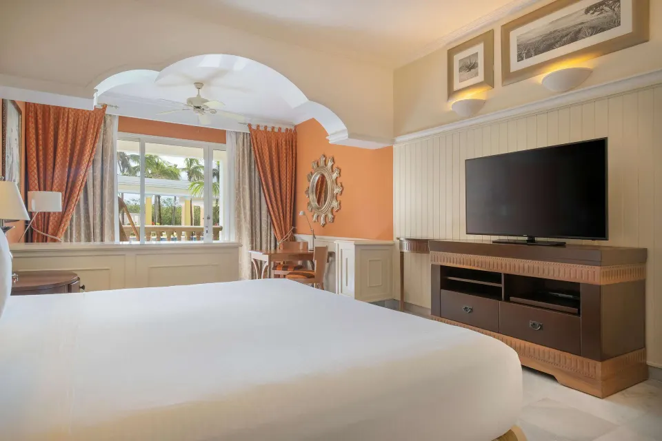 Suite bedroom with a king bed, TV, desk, and balcony at JOIA Paraíso by Iberostar.