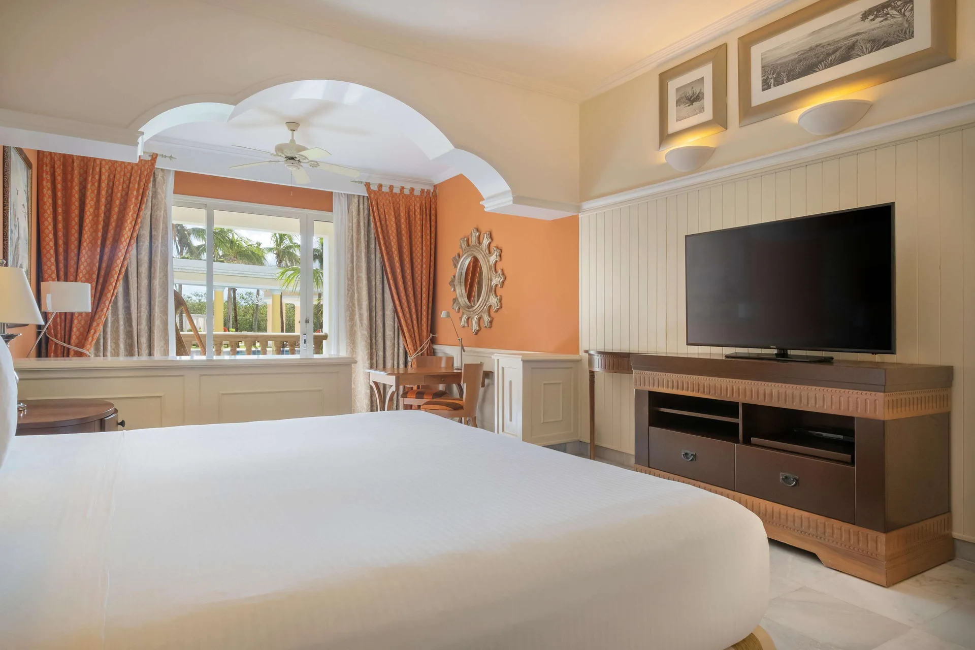 Suite bedroom with a king bed, TV, desk, and balcony at JOIA Paraíso by Iberostar.