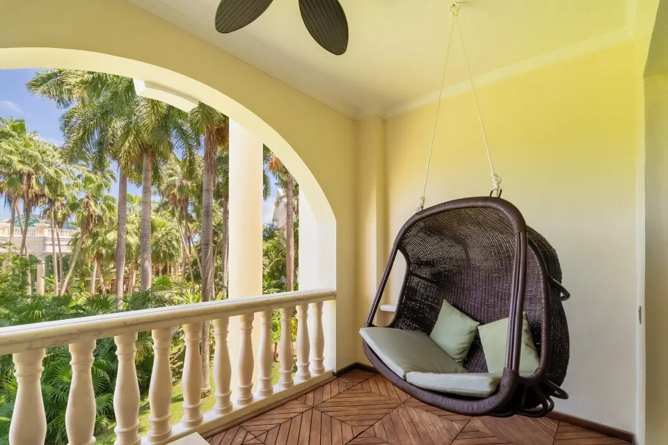 Suite terrace with hanging wicker chair and palm garden view at JOIA Paraíso by Iberostar.
