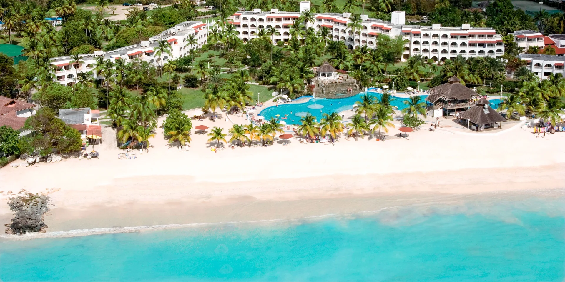 Aerial beachfront view of resort buildings and pool at Jolly Beach Antigua.