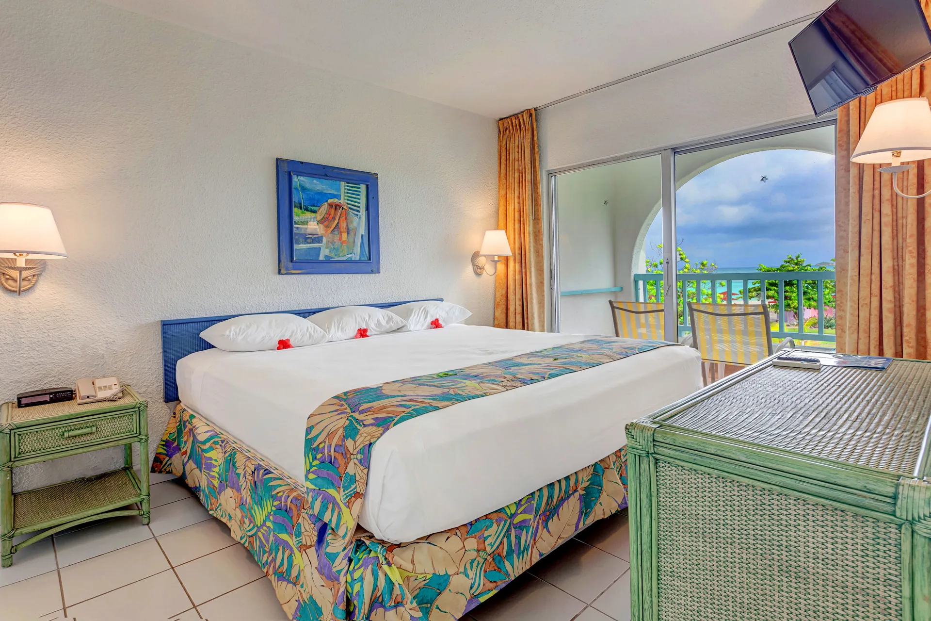 King bed guest room with balcony seating and ocean glimpse at Jolly Beach Antigua.