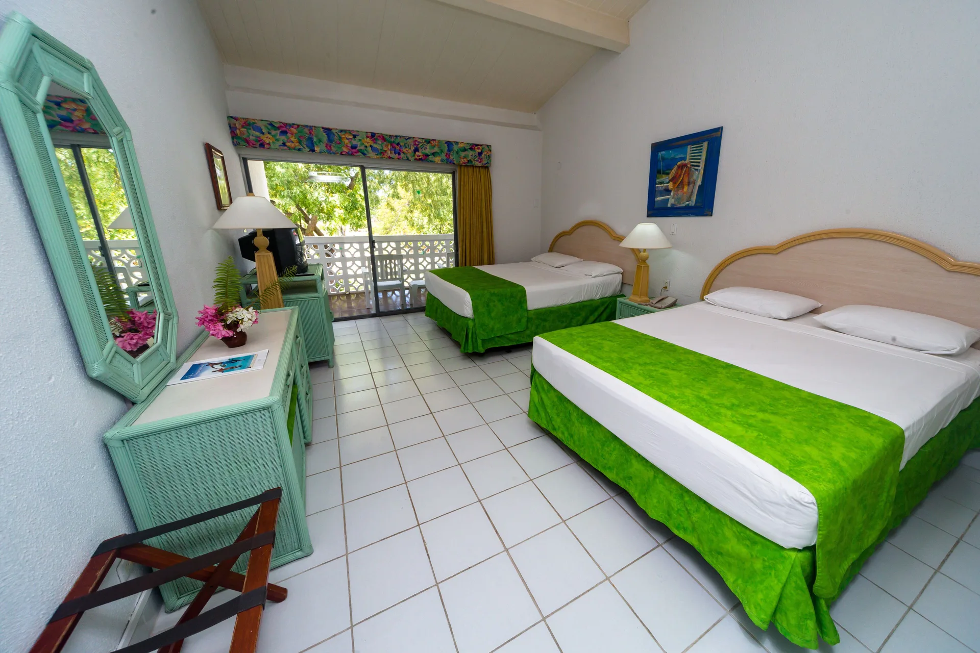 Two-bed guest room with dresser, mirror and balcony at Jolly Beach Antigua.