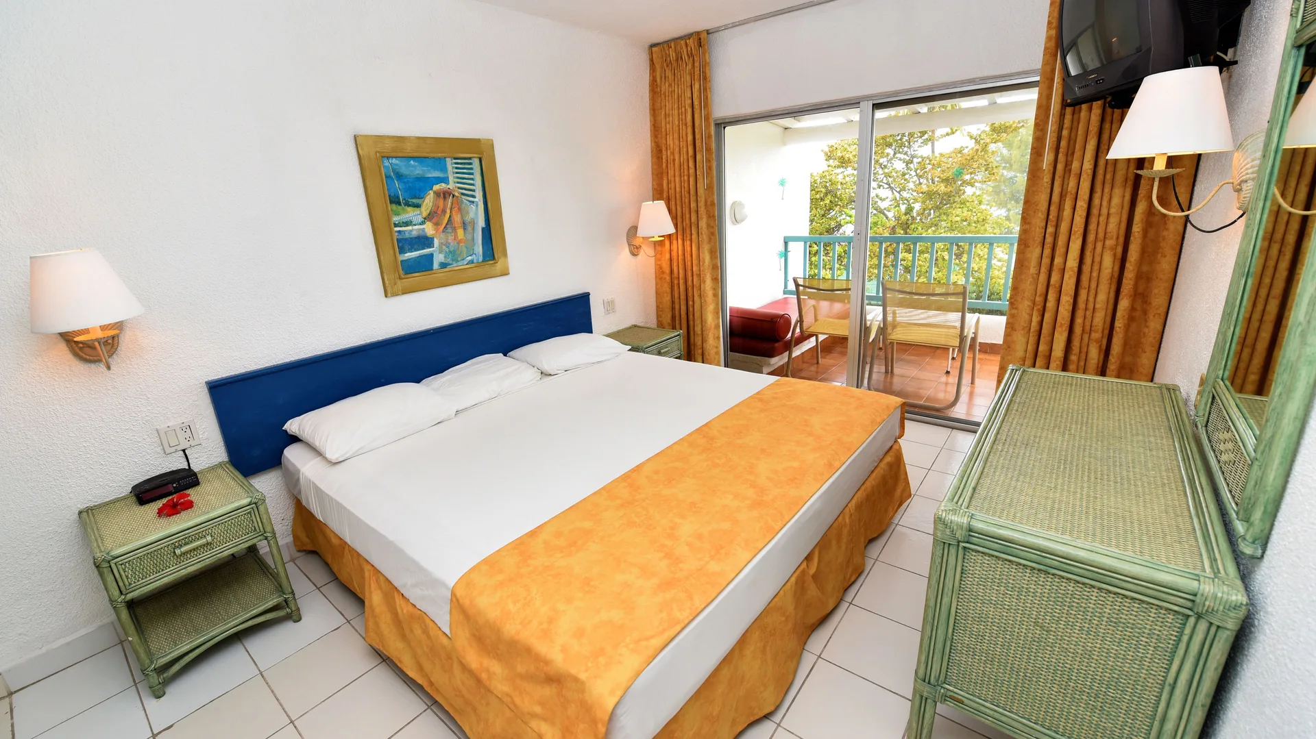 Guest room with king bed, balcony doors, and wicker furniture at Jolly Beach Antigua.