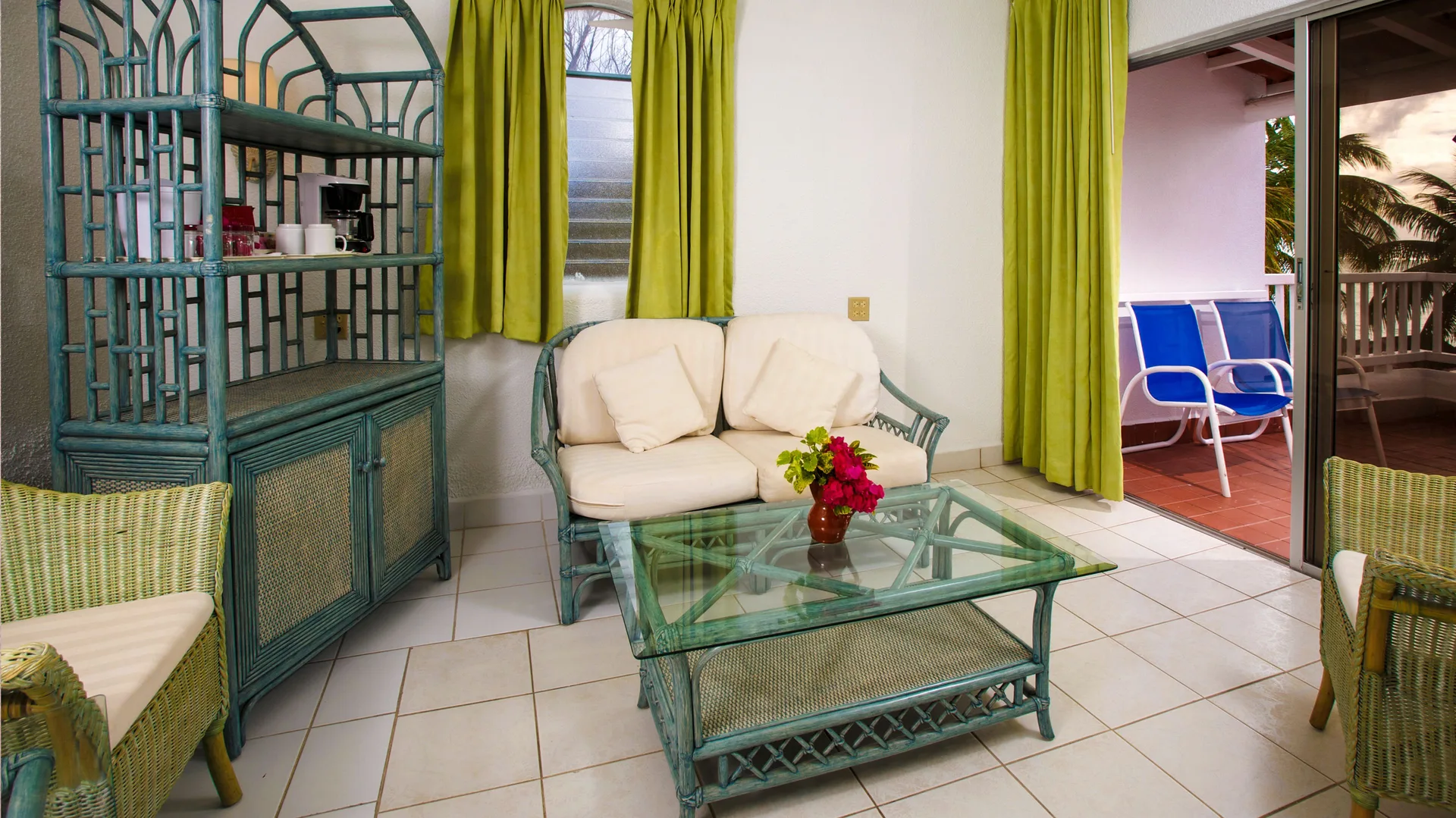 Guest room sitting area with wicker furniture and balcony at Jolly Beach Antigua.