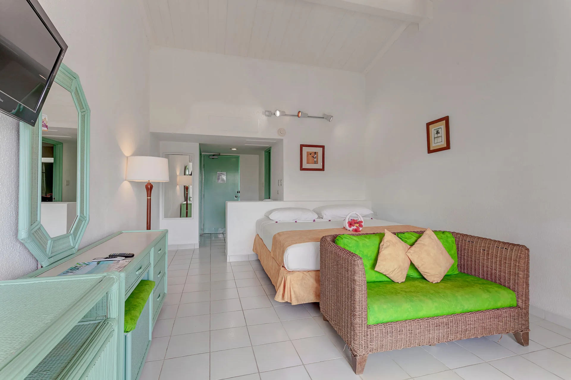 Guest room with two beds, green sofa, dresser, and wall-mounted TV at Jolly Beach Antigua.