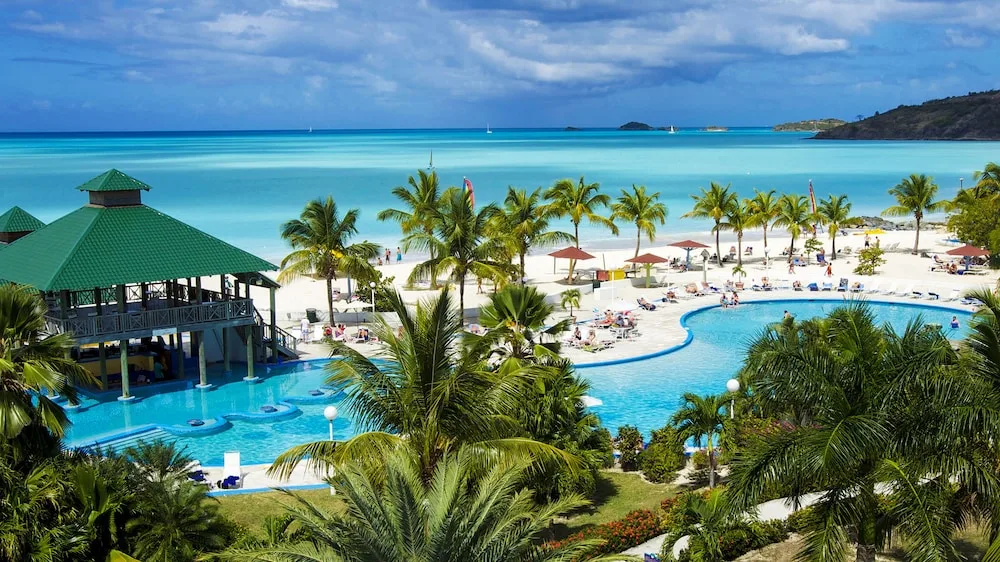 Pool, palms, and white-sand beach overlooking the sea at Jolly Beach Antigua.