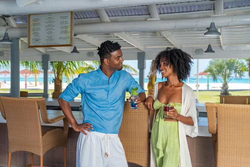 Couple holding drinks at an open-air beach bar at Jolly Beach Antigua.