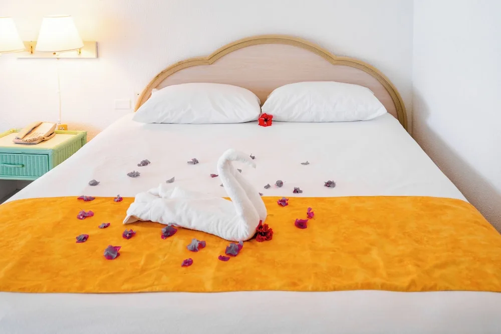 Standard Room at Jolly Beach Antigua with a king bed, yellow runner, petals, and towel swan.