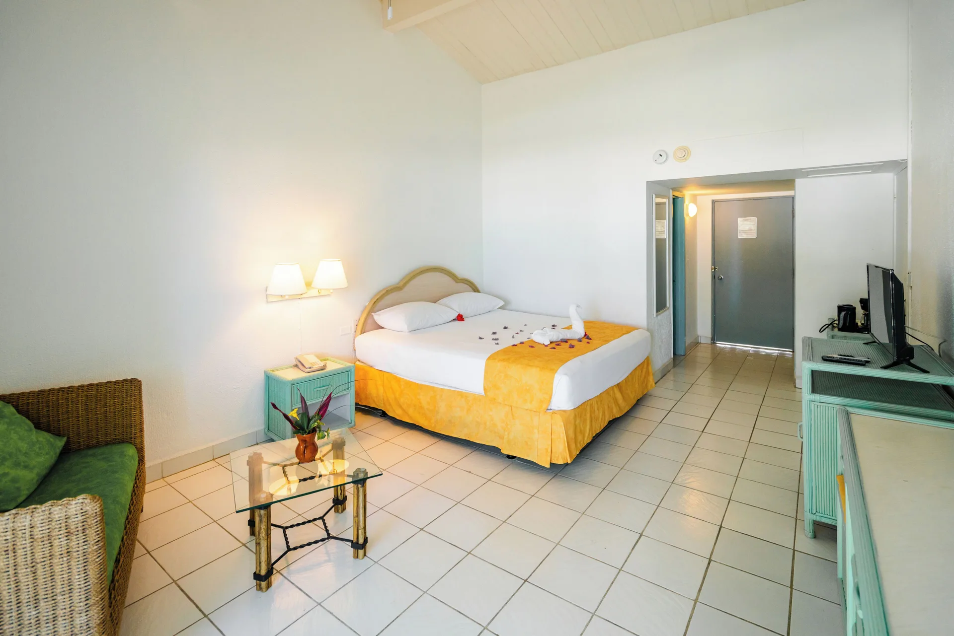 Standard Room at Jolly Beach Antigua with a king bed, sitting area, TV, and tiled floor.
