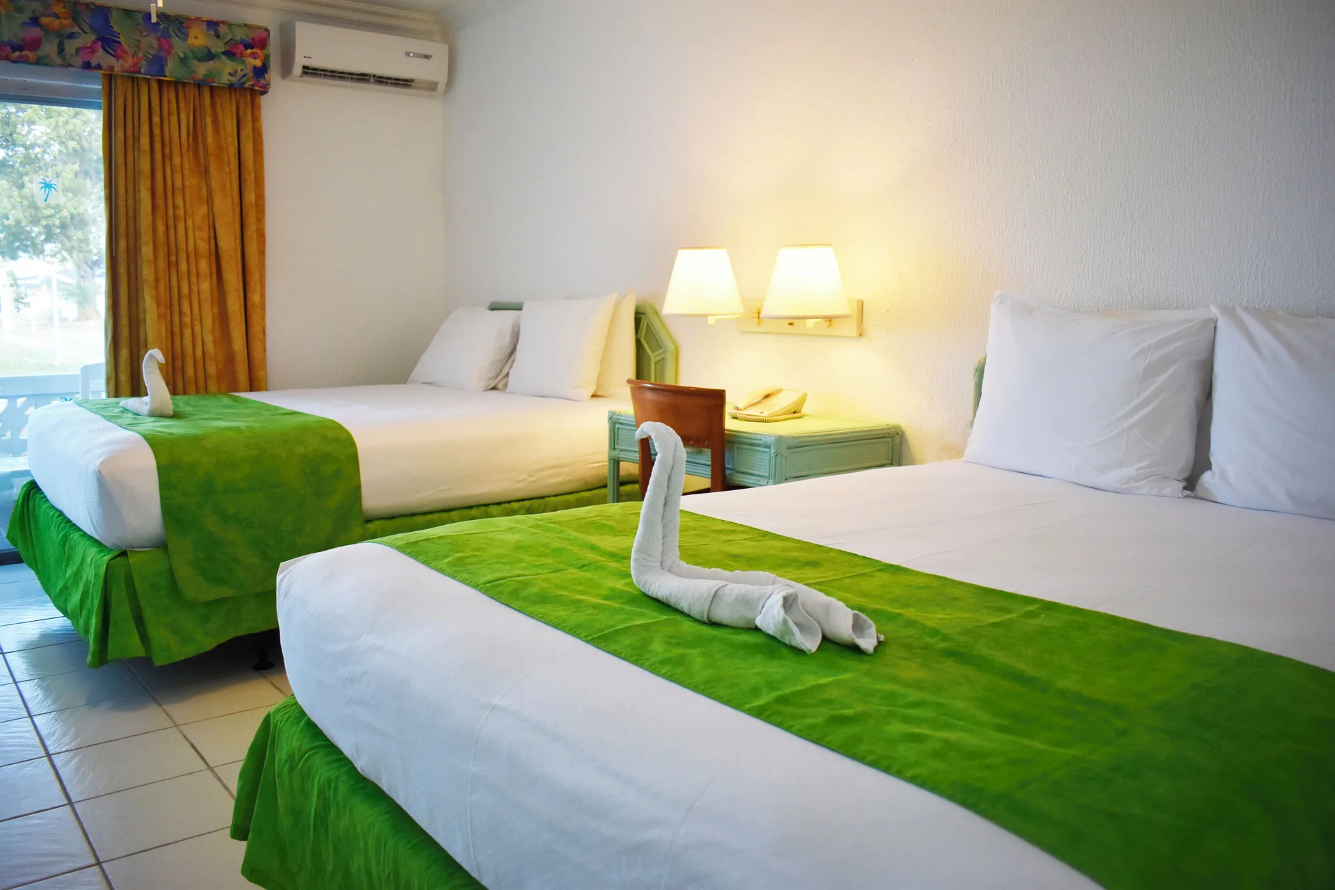 Standard Room at Jolly Beach Antigua with two beds, green runners, towel swans and a window.