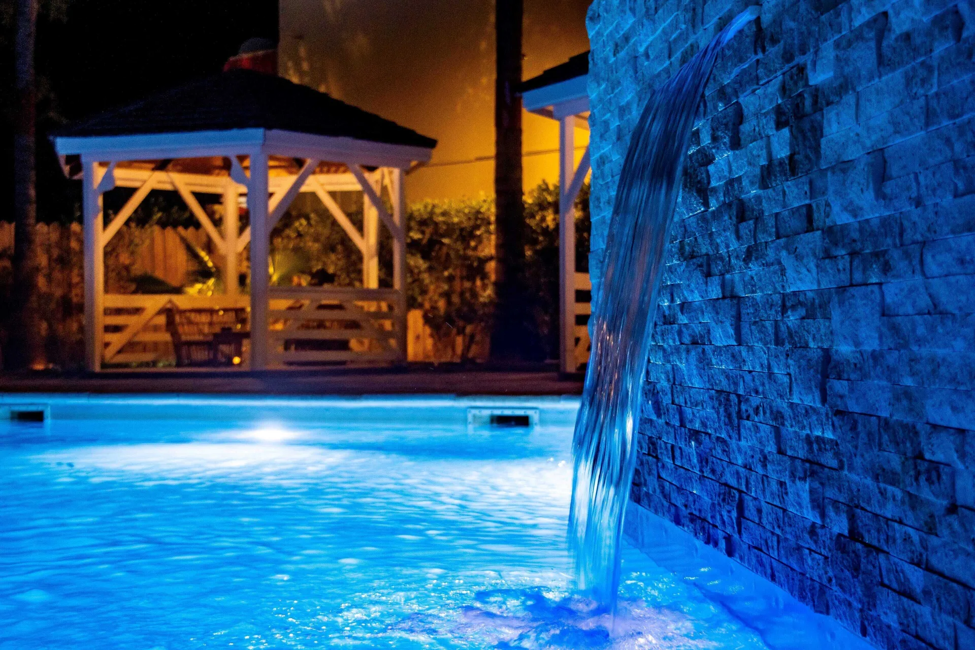 Nighttime pool waterfall glowing blue with a gazebo in the background at La Playa Orient Bay.