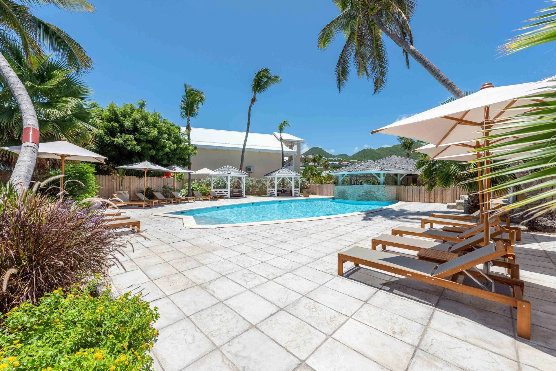 Pool terrace with loungers, umbrellas, palms and cabanas at La Playa Orient Bay.