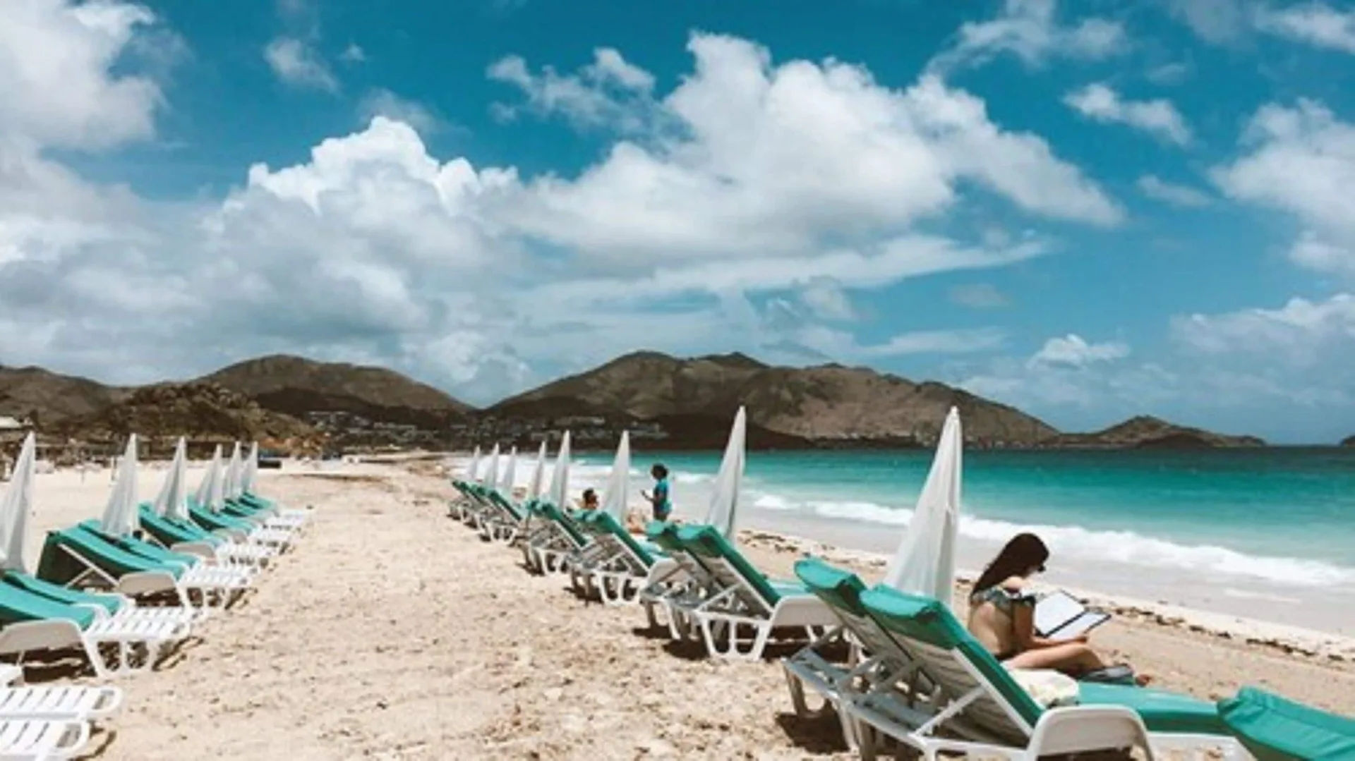 Beach loungers facing turquoise water and hills at La Playa Orient Bay.
