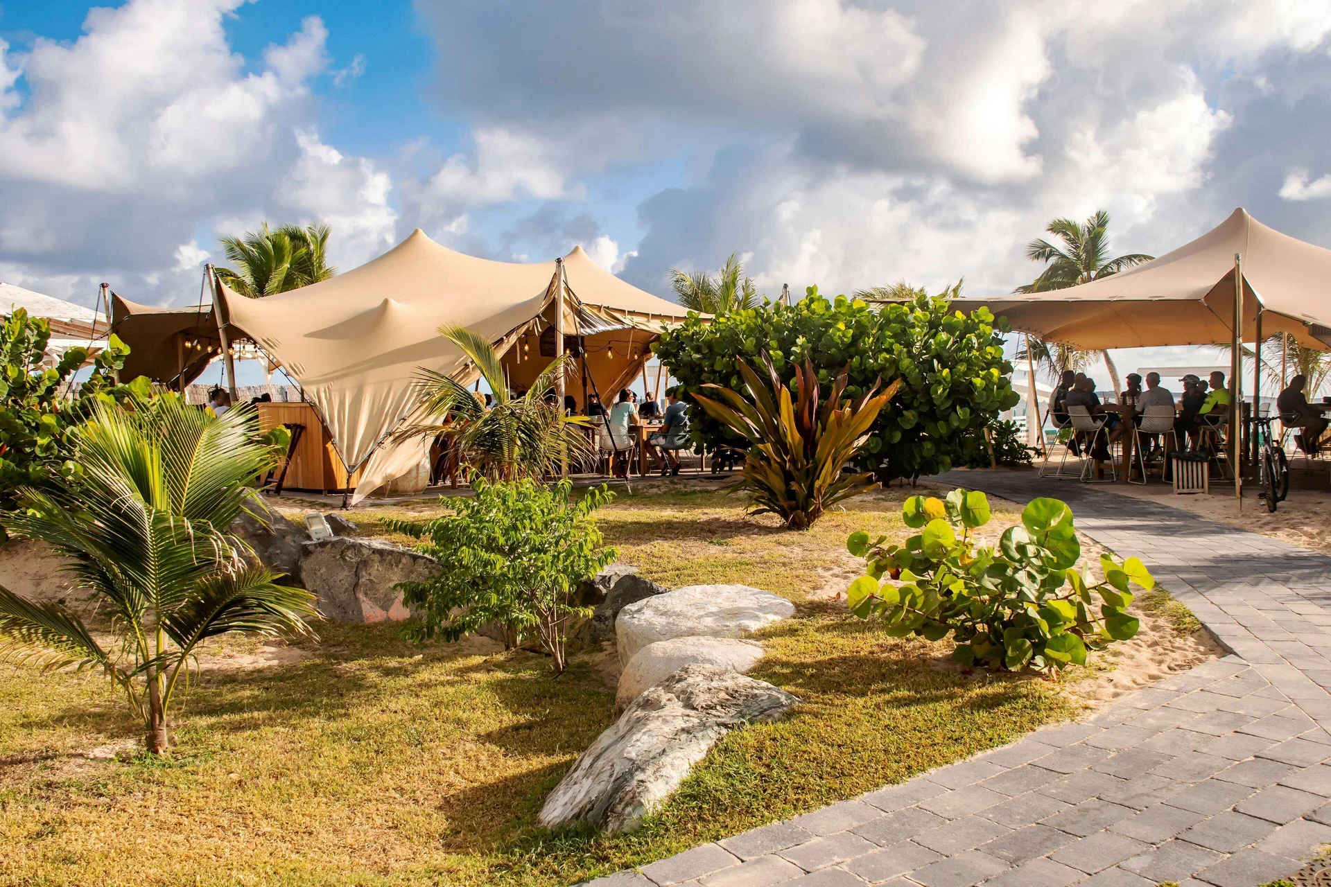 Outdoor beach tents with seated guests, landscaping and walkway at La Playa Orient Bay.