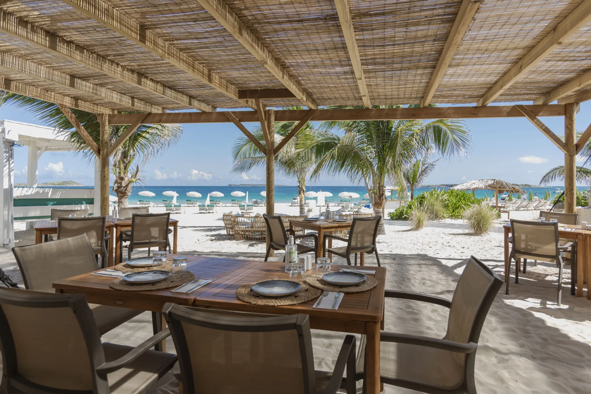 Open-air beachfront dining tables under a woven roof at La Playa Orient Bay.