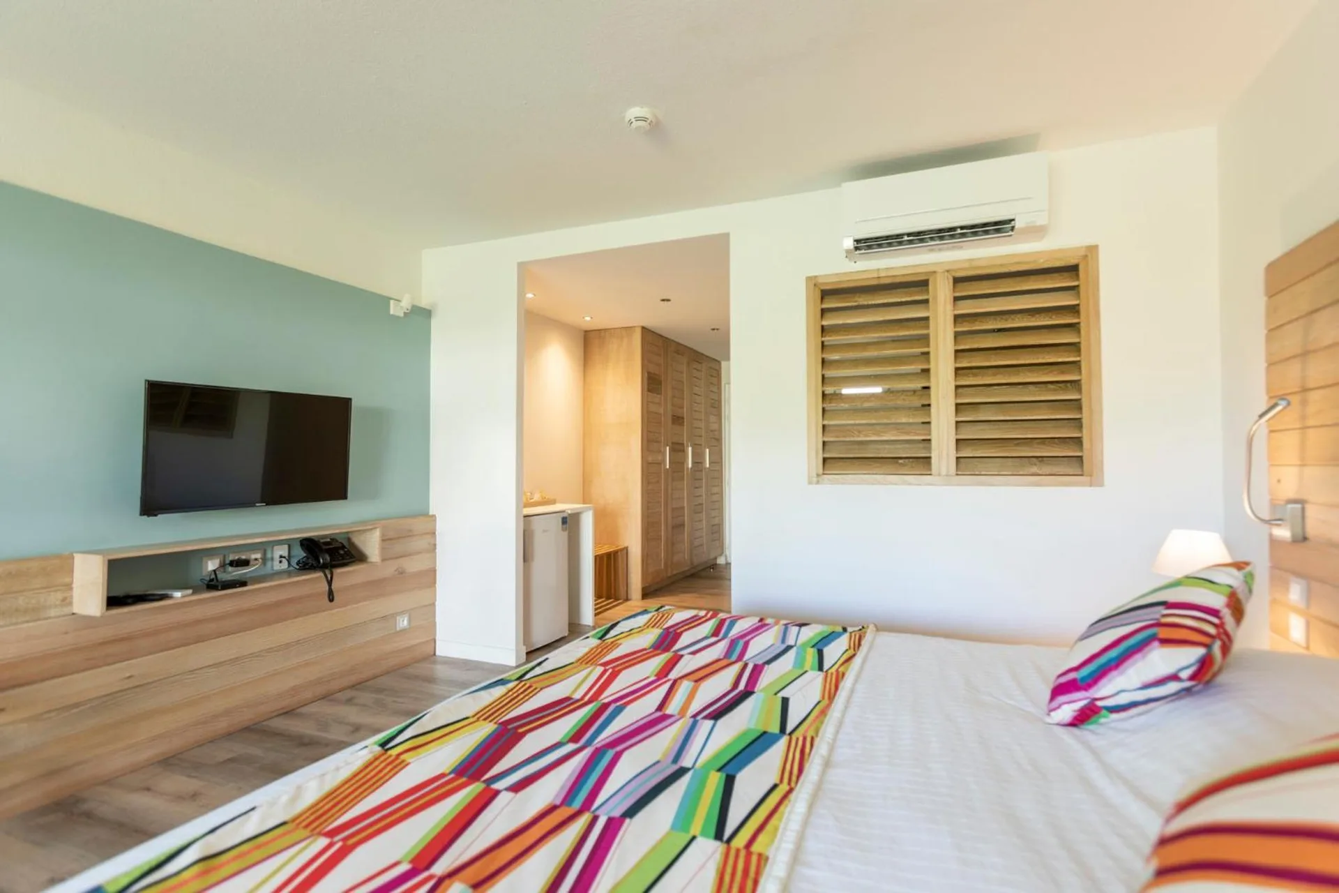 Classic Junior Suite king bed at La Playa Orient Bay facing a wall-mounted TV and entry area.