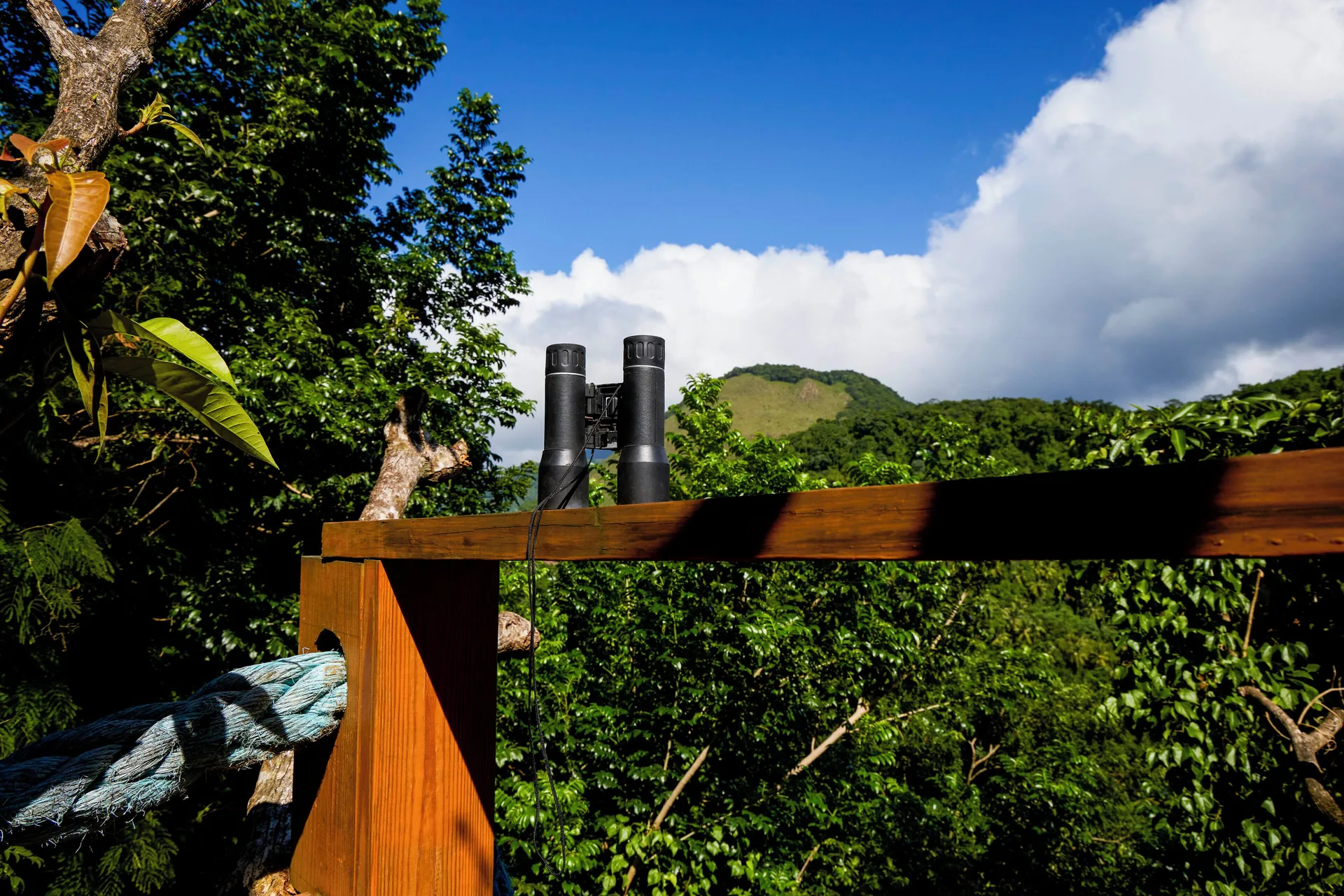 Binoculars on a wooden railing overlooking tropical hills at Ladera Resort.