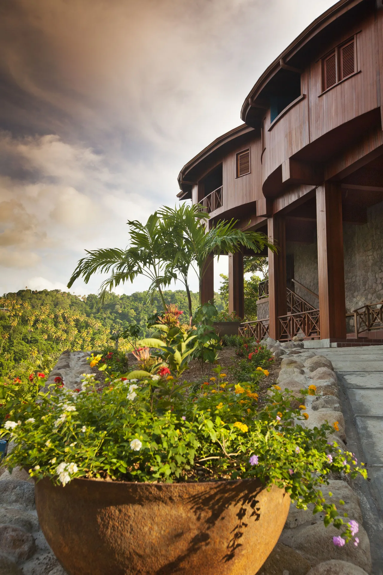 Exterior of suites at Ladera Resort with tropical flowers, palms, steps, and wooden balconies.