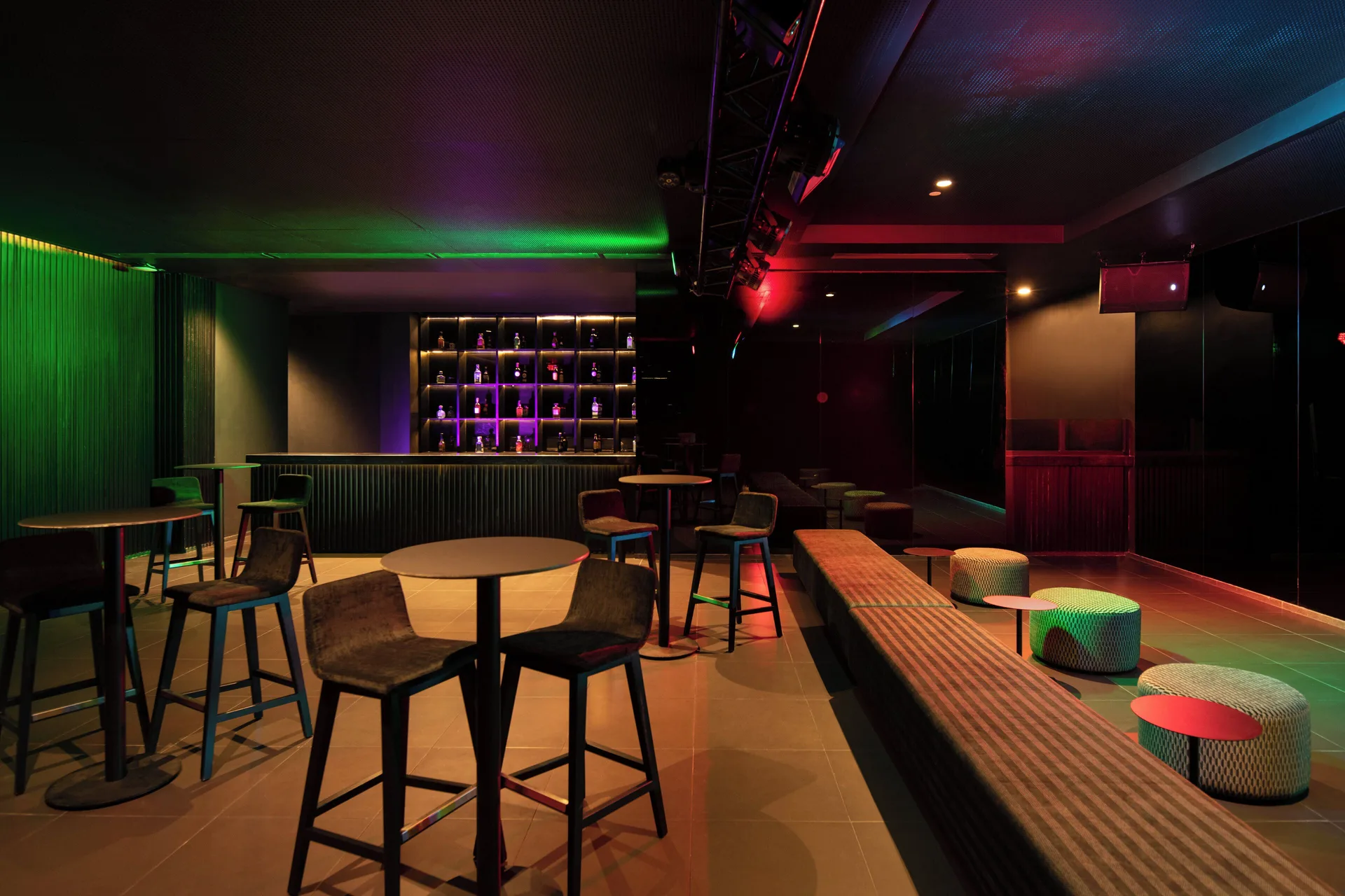 Dim lounge bar with colorful lighting, stools, and bottle shelves at Live Aqua Punta Cana.