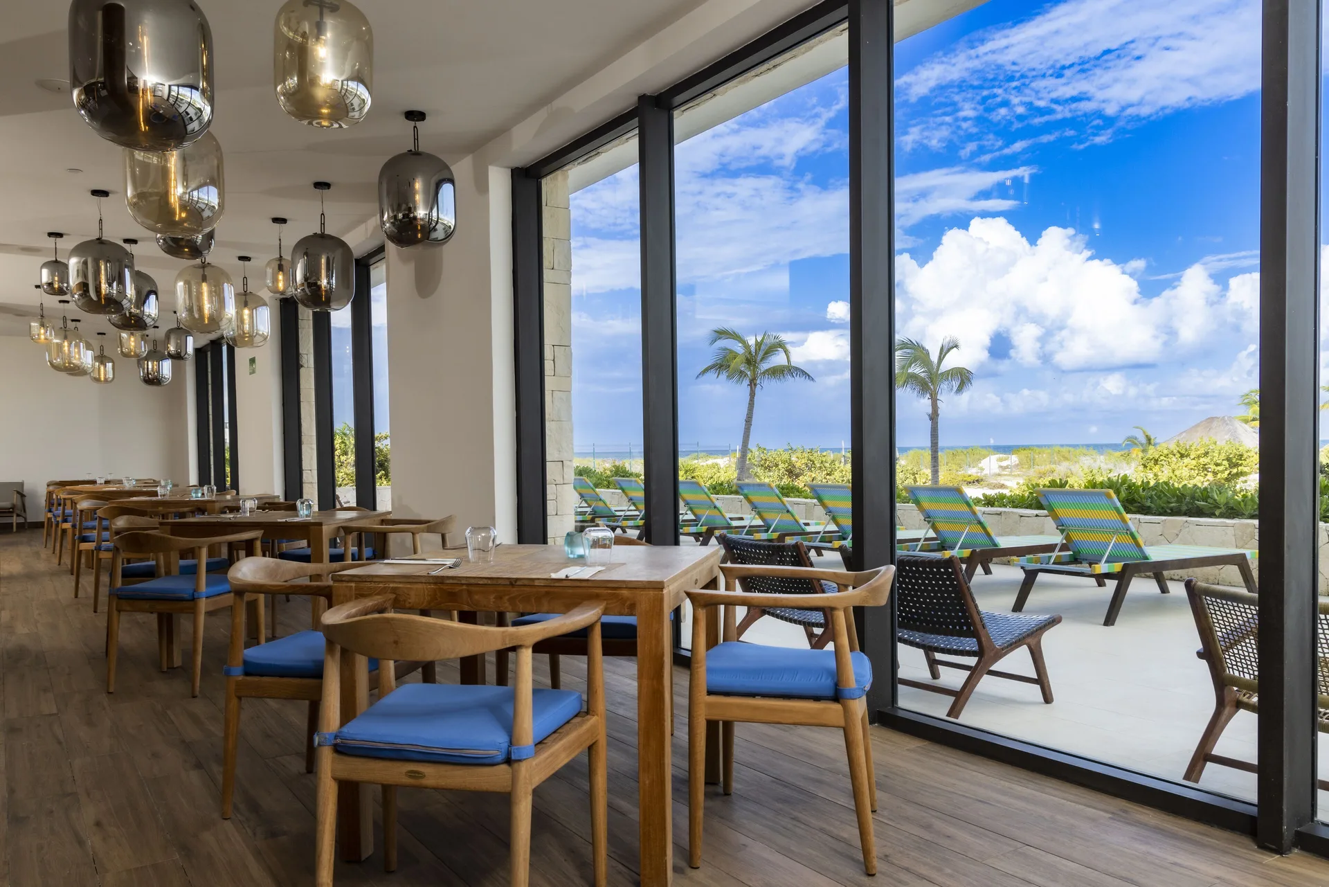 Ocean-facing dining room with blue-cushioned chairs at Majestic Elegance Costa Mujeres.